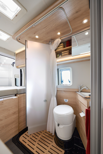Perfekcyjne wykorzystanie przestrzeni dzięki obrotowym drzwiom prysznicowym z matowym przeszkleniem i brodzikiem pod tylnym łóżkiem.
